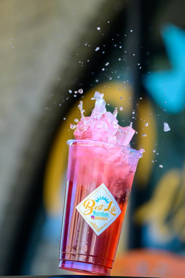 A pink iced drink splashing out of a Best Life Nutrition cup